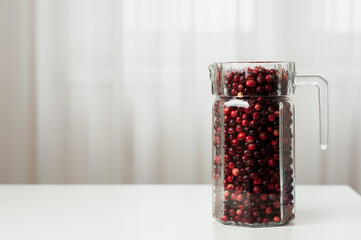 Cranberry. Small forest red berry. Cranberries in a jug and in a glass on the table. A glass of cranberries. Vitamins from nature. Selective focus.