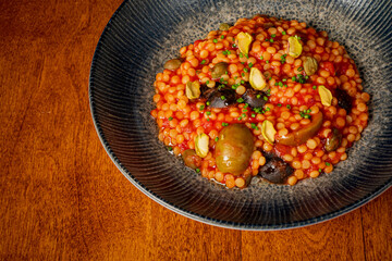 Pearl couscous is artfully arranged with a rich tomato sauce and garnished with olives and nuts