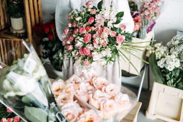 Florist holding a finished bouquet of mixed pink flowers including roses and alstroemeria in a flower studio The art of bouquet composition, floral design process, handmade floristry, studio practice