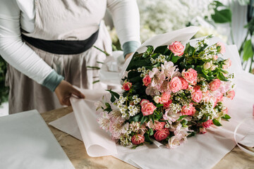 Floral bouquet of pink roses, alstroemeria, and babys breath laid on white paper before final wrap....