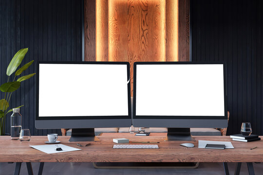 Dual monitor mockup on wooden workstation in backlit modern office interior with blank screens for design or branding presentation template. 3D Rendering