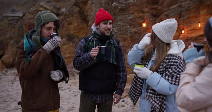 Friends drinking a hot drink from a cup during their hike near a cliff in winter