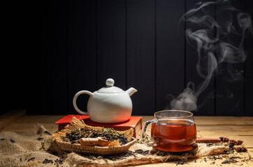 Hot tea in teacup with steam. Herbal tea glass placed on rustic wooden table on dark background.