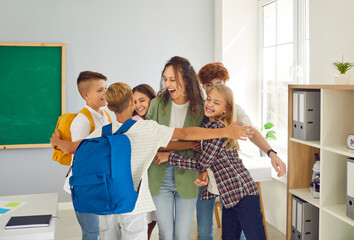 Children meet their favorite teacher after long vacation. Group of joyful schoolchildren hug female...