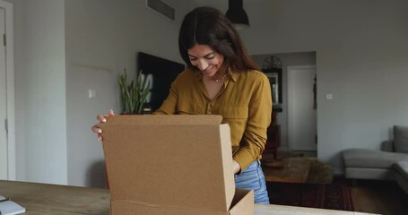 Woman stand at table opening large cardboard box with positive expression, enjoy received gift, got surprise or bought goods for home. Electronic commerce, webstore client, express transport services
