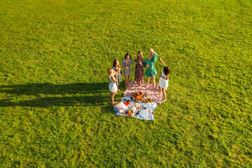 Drone aerial view with a group of young women dancing in nature at a picnic in the evening