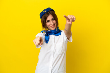 Airplane stewardess woman isolated on yellow background points finger at you while smiling