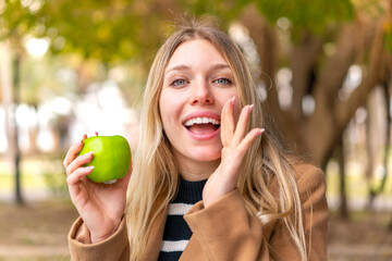 Young pretty blonde woman with an apple at outdoors shouting with mouth wide open
