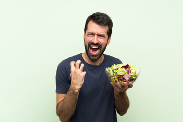 Young handsome man with salad over isolated green wall frustrated by a bad situation