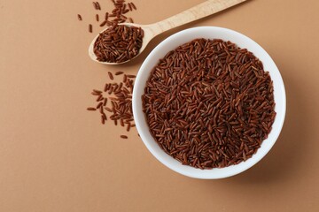 Raw brown rice in bowl on color background