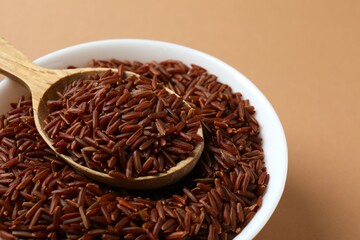 Raw brown rice in bowl on color background