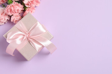 Beautiful bouquet of pink carnations with gift box on a color background
