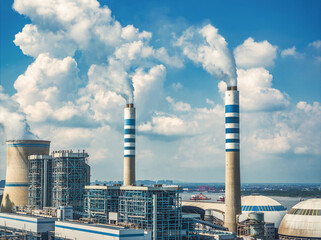 Close up view of industrial power plant chimneys emitting smoke steam against blue sky with white...