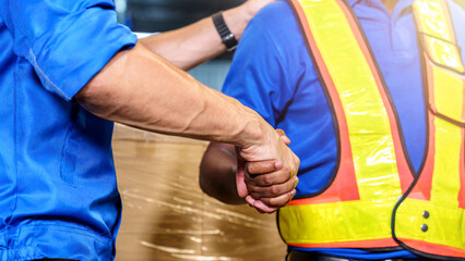 Two warehouse workers shaking hand in a storage warehouse.