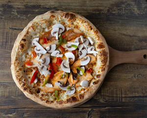 Overhead view of a mushroom and chicken pizza on a wooden board table