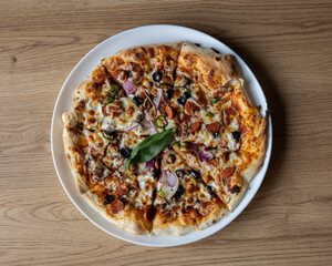 Overhead shot of a fully topped pizza on a white plate on wood table