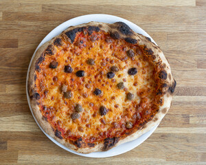 Overhead shot of a pizza with olives and sausage on a white plate