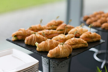 A beautifully arranged tray of freshly baked croissants alongside delicious sandwiches is displayed enticingly on a table