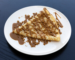 Close up of crepe with chocolate sauce and cookie crumbs on white plate