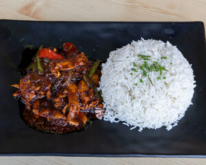Spicy Asian chicken with basmati rice on black plate for fusion lunch visuals