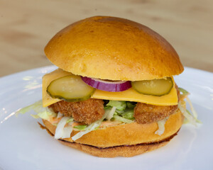 Close up of a chicken sandwich with cheese and pickles on a white plate