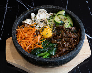 Traditional Korean bibimbap with beef, vegetables and raw egg in hot stone bowl for Asian cuisine visuals