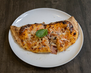 Folded pizza slice with ham, cheese and basil on white plate for rustic Italian meal visuals