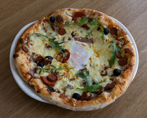 Close up of a pizza with egg sausage olives and arugula on a white plate