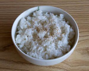 Close up of a bowl of white rice topped with sesame seeds on a table