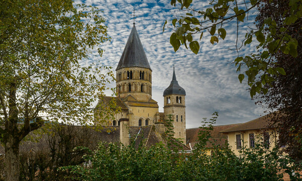 Die Abtei Cluny im Burgund vor einem Wolkenhimmel, eingerahmt von B&auml;umen