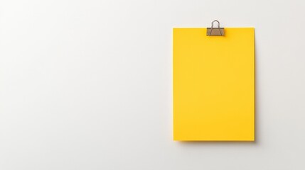 A bright yellow notepad is clipped to a plain wall, symbolizing creativity and ideas waiting to be explored.