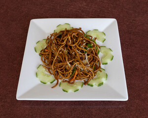 A square plate filled with noodles and cucumber slices arrangement