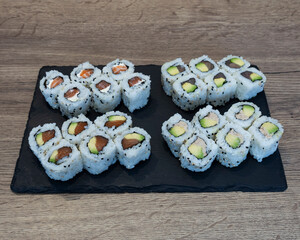 Various sushi rolls arranged on a black slate board on wooden surface