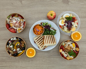 Assortment of salads with panini and fruits on a wooden table top