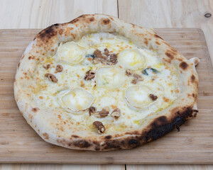 Close up shot of a gourmet pizza with cheese and walnuts on wood board