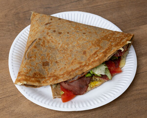 Close up of a savory crepe filled with meat and vegetables on a plate