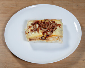 Close up of a crepe on a white plate topped with bacon pieces on wood