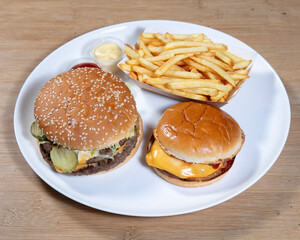 Two burgers and fries on a white plate with condiments on the side view