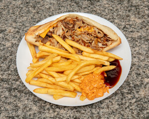 Close up shot of a kebab sandwich with fries and sauces on a plate