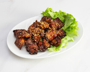 Close up of glazed pork pieces with sesame seeds on a white plate