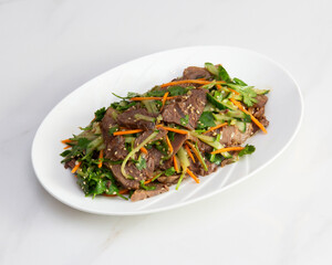 Close up of a beef salad on a white plate with carrot and cucumber