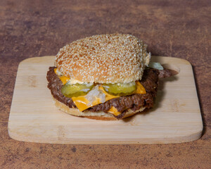 A cheeseburger with pickles on a wooden board ready to be devoured