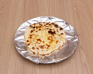 Freshly baked naan bread on aluminum foil on a wooden table surface
