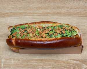 Close up of a gourmet hotdog with avocado and crispy fried onions on wood