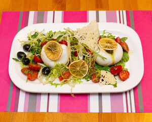Burrata salad with tomatoes olives and lemon on a white rectangular dish
