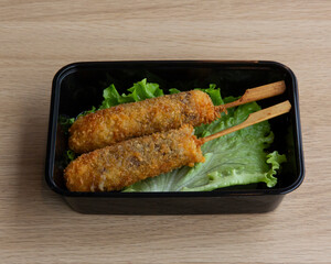 Two fried skewers served over lettuce in a black container on a table
