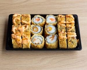 Assorted fried sushi rolls arranged on a black plastic container tray