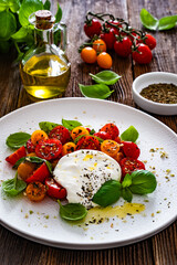 Caprese salad - tomatoes, fresh basil leaves and burrata cheese on wooden background	