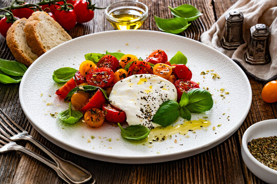 Caprese salad - tomatoes, fresh basil leaves and burrata cheese on wooden background	