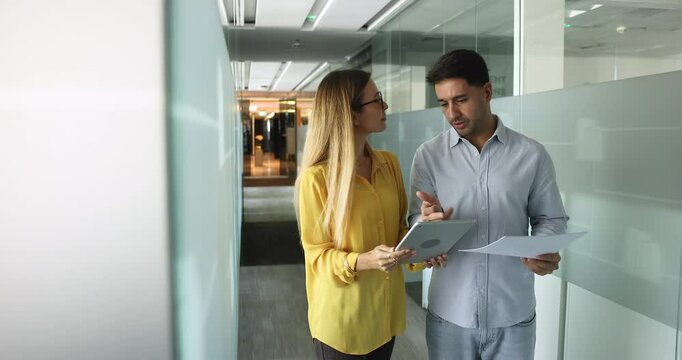 Young female project manager consulting male professional colleague, showing online content on tablet to coworker man, asking for job advice, consultation, corporate help, support